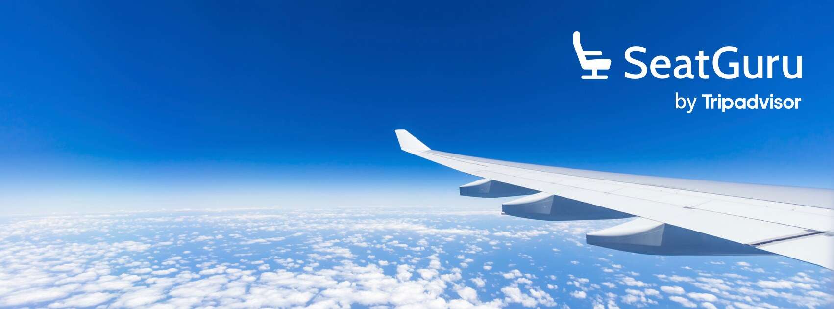View of airplane wing flying above clouds in clear blue sky.